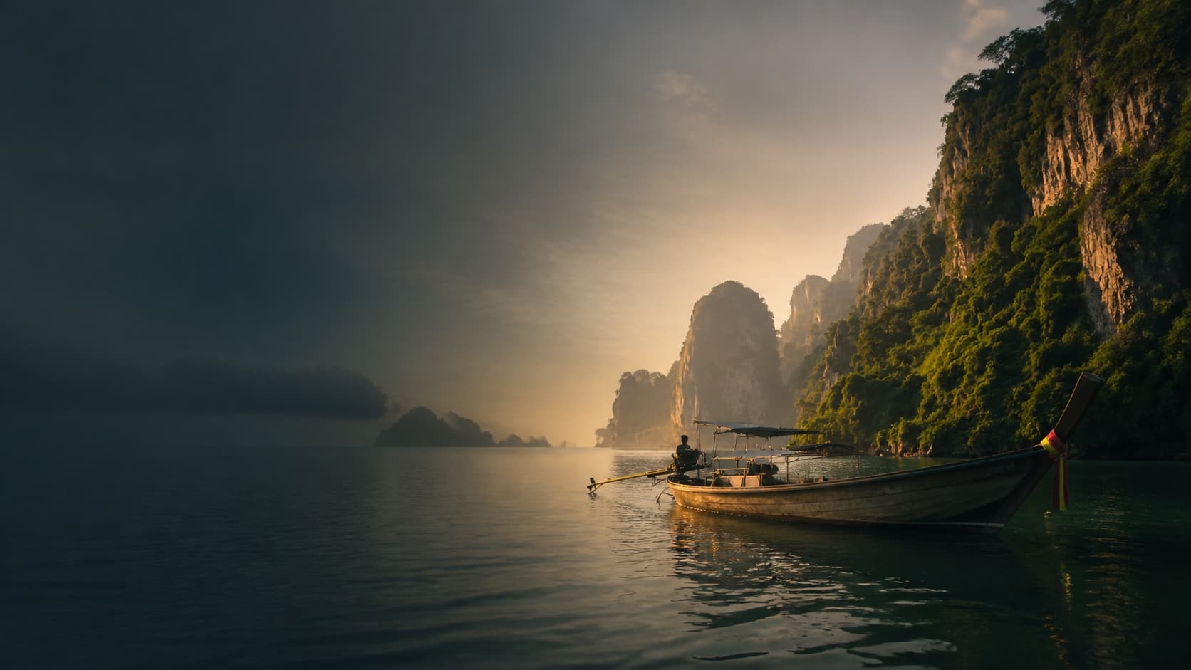 A traditional longtail boat beneath limestone cliffs at dawn in Thailand.